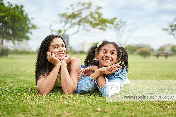 Portrait happy brunette mother and daughter laying in park grass
