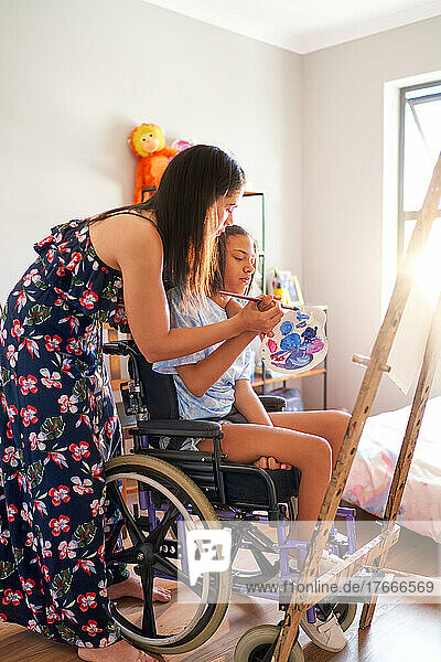 Mother and disabled daughter in wheelchair painting at home