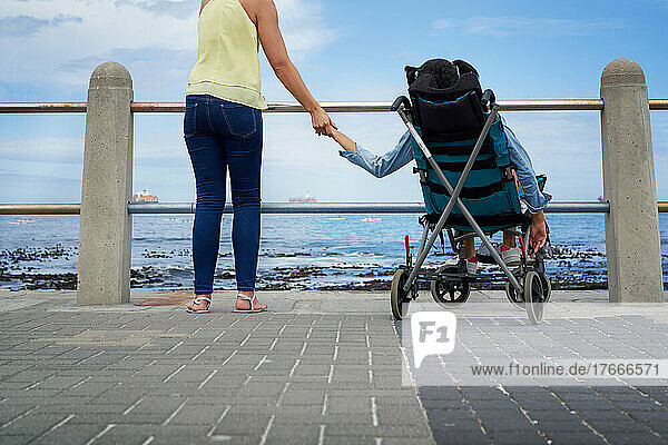 Mother holding hands with disabled daughter in pushchair at beach