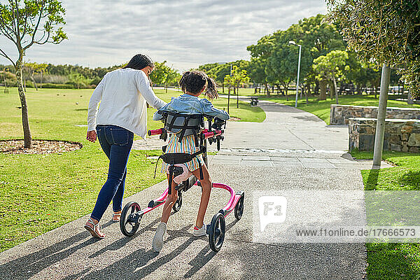 Mother and disabled daughter with rollator walking in sunny park