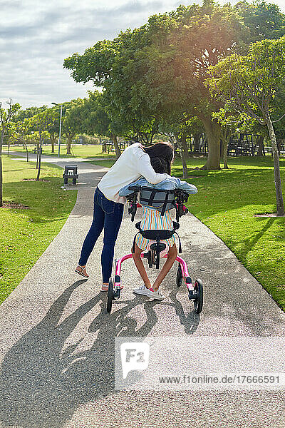 Affectionate mother hugging daughter in rollator at sunny park