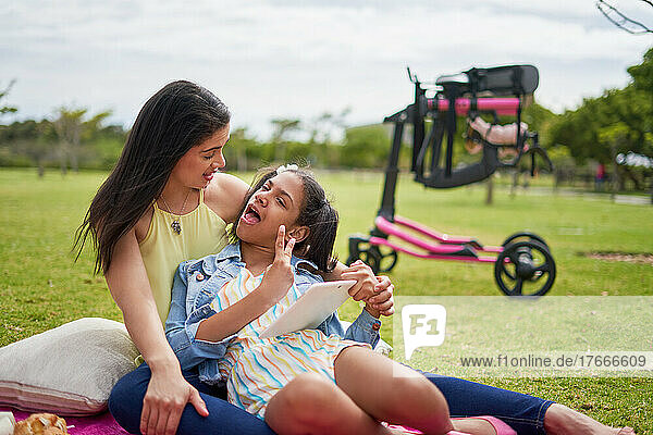 Mother and disabled daughter with digital tablet on blanket in park