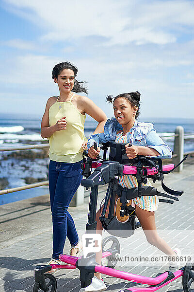 Mother and disabled daughter with rollator walking on sunny boardwalk