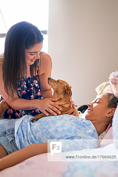 Mother  disabled daughter and cute dog cuddling on bed at home