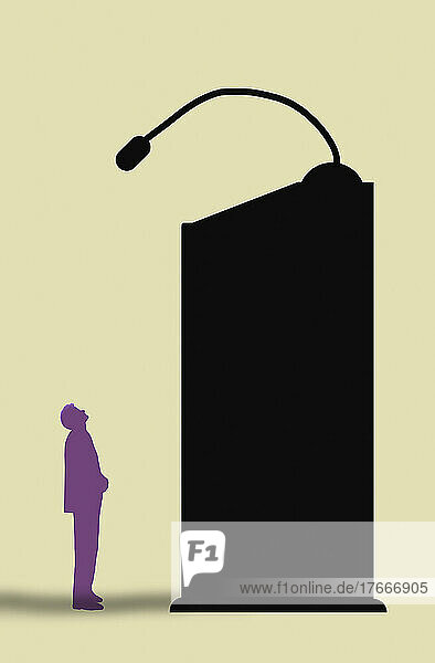 Kleiner Mann blickt von einem hohen Rednerpult auf ein Mikrofon