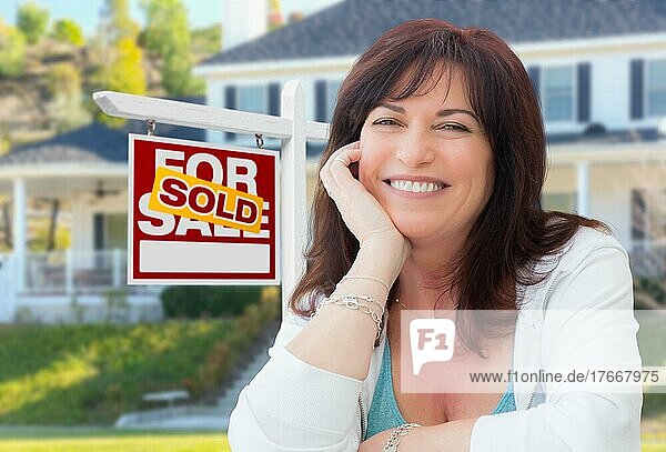 Frau mittleren Alters vor einem Haus mit einem zum Verkauf stehenden Immobilienschild im Hof