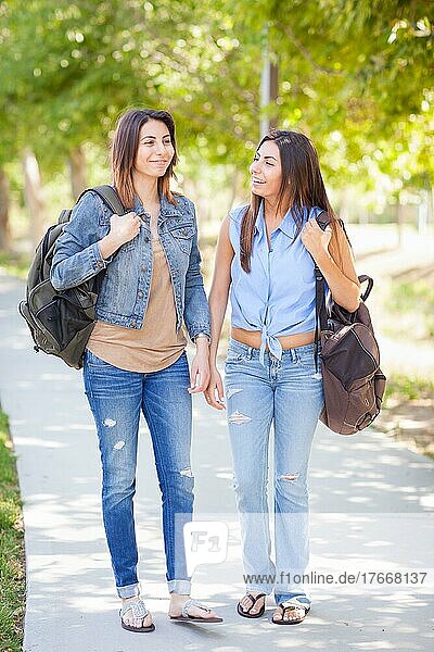 Zwei schöne junge ethnische Zwillingsschwestern mit Rucksäcken gehen im Freien