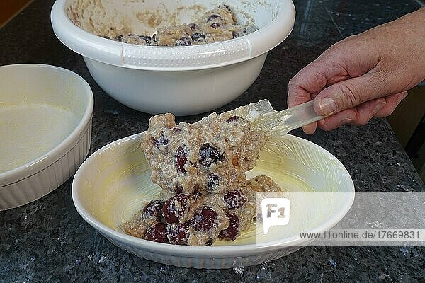Swabian cuisine  putting bread rolls and cherry mixture into a casserole dish  preparing simple cherry pastry  poor people's food  using leftovers  dessert from the oven  casserole with stale bread rolls  stale bread  baking  baked goods  mixing bowl  dough scraper  man's hand  traditional cuisine  food photography  studio  Germany  Europe
