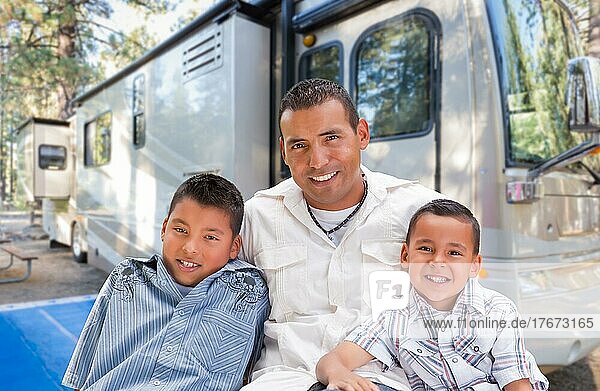 Glücklicher hispanischer Vater und seine Söhne vor ihrem schönen Wohnmobil auf dem Campingplatz