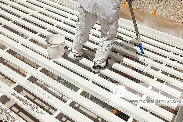 Professional painter rolling white paint onto the top of A home patio cover