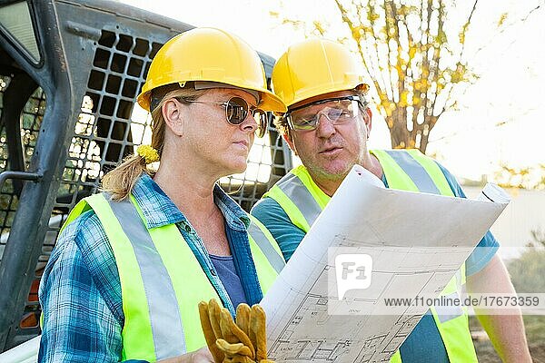 Männliche und weibliche Arbeiter mit technischen Plänen im Gespräch auf der Baustelle