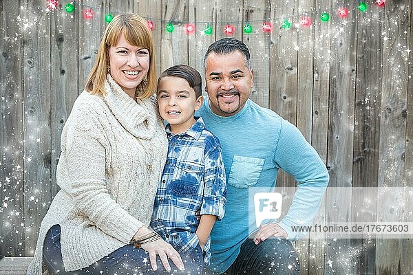 Glückliche junge gemischtrassige Familie Porträt außerhalb mit Weihnachtsbeleuchtung und Schnee-Effekt