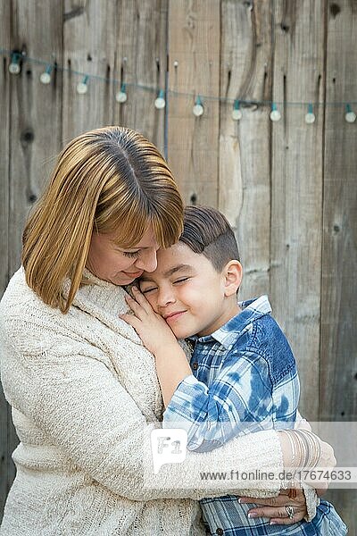 Liebevolle Mutter und gemischtrassiger Sohn umarmen sich am Zaun