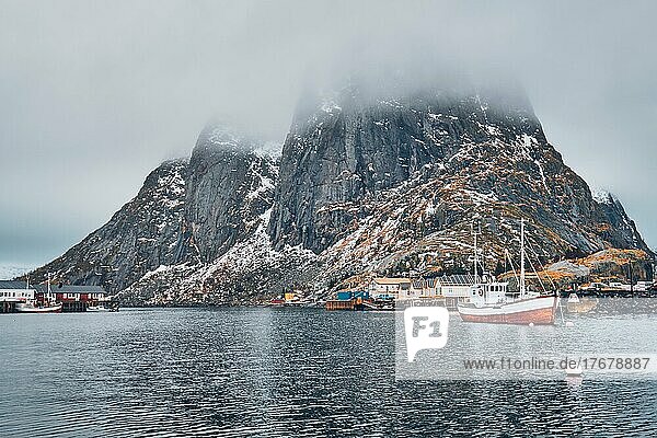 Ein Fischerboot im Fischerdorf Hamnoy auf den Lofoten  Norwegen  mit roten Rorbu-Häusern. Mit fallendem Schnee  Europa