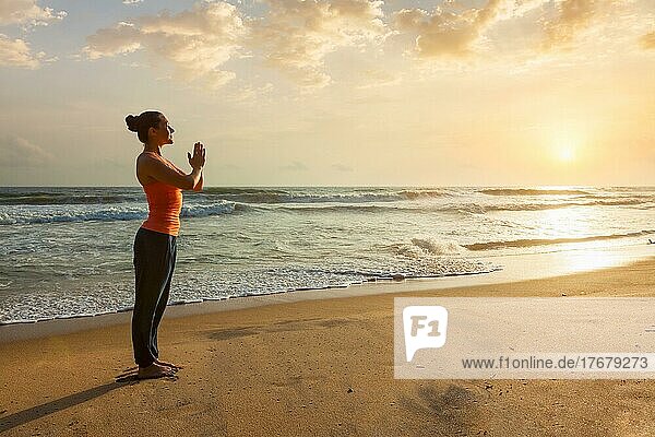 Frau macht Ashtanga Vinyasa Yoga asana Tadasana Samasthiti Yoga-Haltung am Strand bei Sonnenuntergang