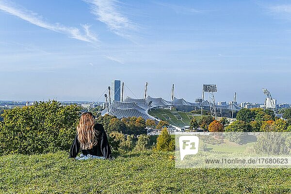 Young woman sitting in the grass  park with Olympic lake and Olympic stadium  Olympic Park Munich  Bavaria  Germany  Europe