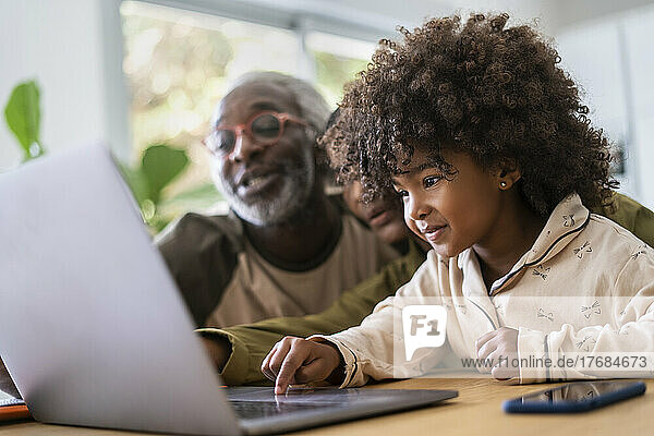Smiling grandparents with granddaughter using laptop