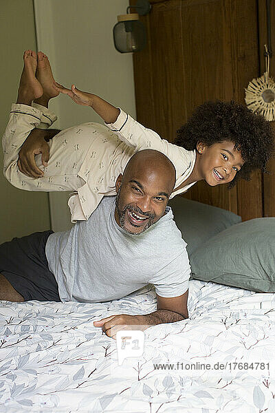 Smiling father carrying his daughter on shoulder in bedroom