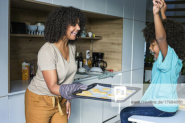 Smiling mother showing her daughter baked cookies in kitchen
