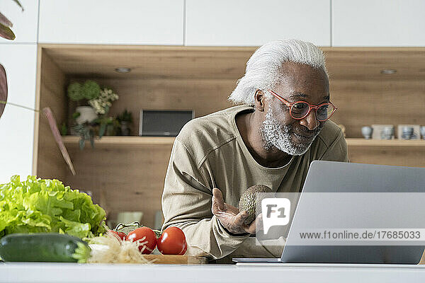 Senior man watching recipe on laptop while leaning on kitchen worktop