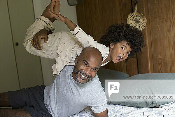 Smiling father carrying his daughter on shoulder in bedroom