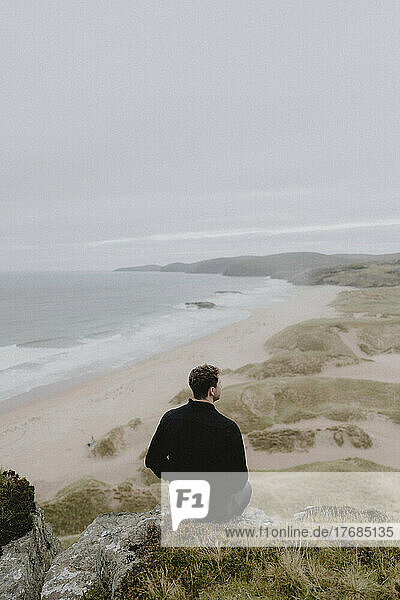 Serene man sitting on cliff overlooking tranquil ocean beach  Sandwood Bay  Assynt  Scotland