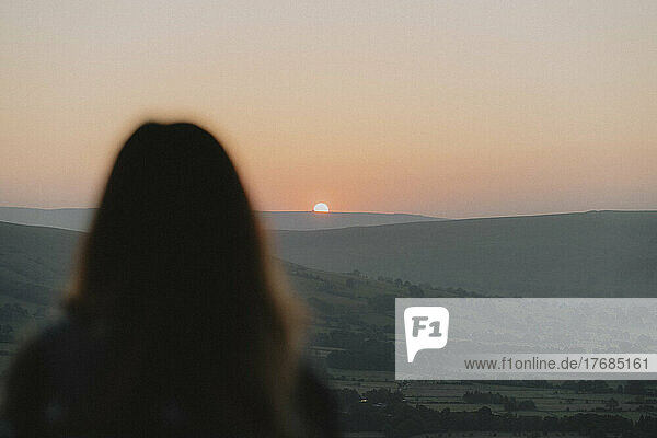 Woman watching sunrise over mountains in distance  Castleton  Derbyshire  England