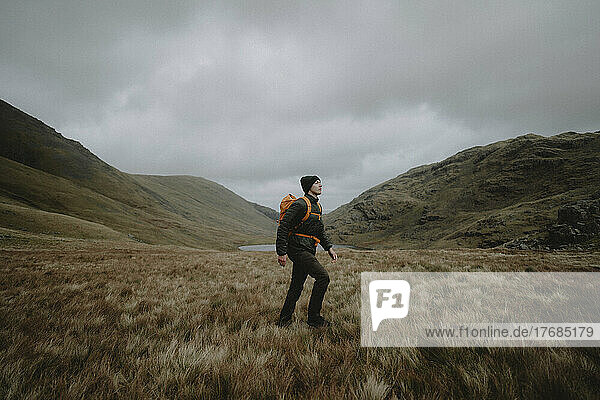 Männlicher Wanderer mit Rucksack wandert unter Hügeln in abgelegener Landschaft  Great End  England