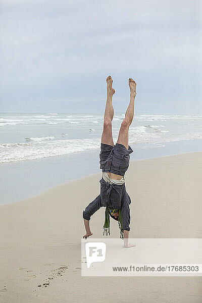 Carefree woman doing handstand on sandy ocean beach
