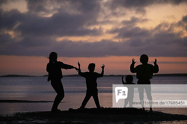 Silhouettierte Familie tanzend  gestikulierend am Meeresstrand bei Sonnenuntergang