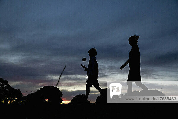 Silhouetted mother and son with ball walking below dusk sky