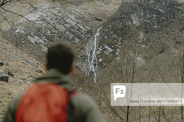 Male hiker watching waterfall on rugged cliff  Glen Nevis  Scottish Highlands  Scotland