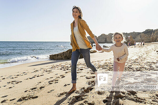 Happy mother with daughter walking on shore at beach