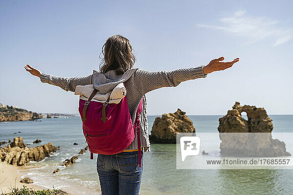 Carefree woman with arms outstretched standing in front of sea