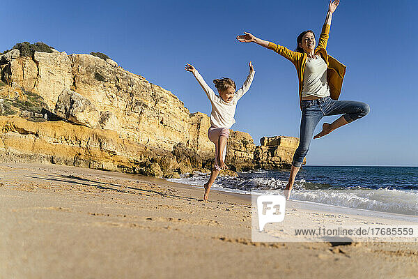 Glückliche Frau mit Tochter springt an einem sonnigen Tag am Strand
