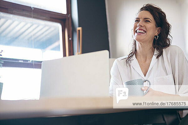 Happy freelancer with coffee cup and laptop working at home