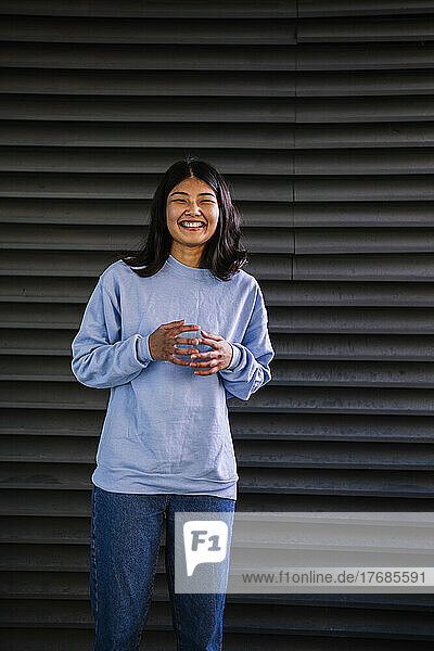 Happy young woman standing in front of corrugated iron shutter