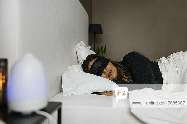 Junge Frau mit Augenmaske schläft zu Hause im Bett