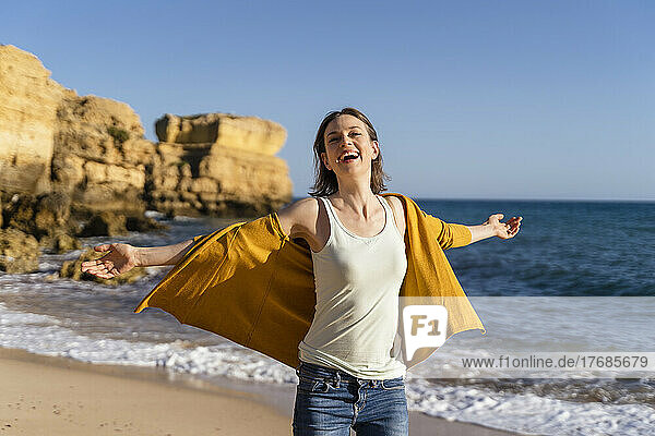 Happy woman with arms outstretched enjoying at beach on sunny day