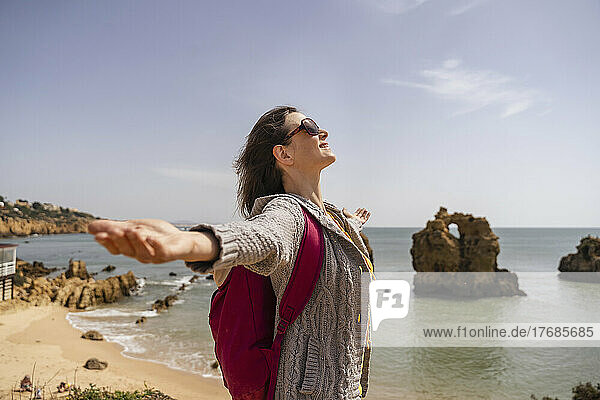 Happy woman wearing sunglasses standing with arms outstretched on sunny day