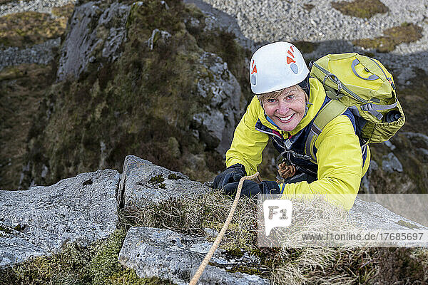 Smiling woman wearing sports helmet climbing rocky mountain