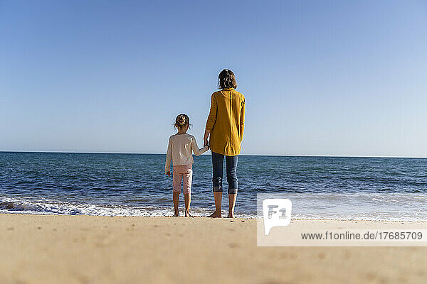 Frau mit Tochter steht am Ufer und blickt auf den Horizont