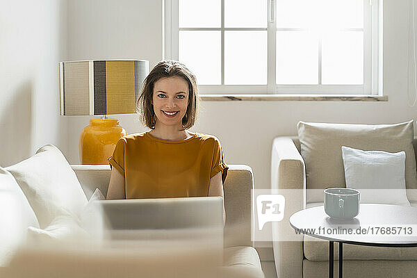 Happy young woman sitting with laptop at home