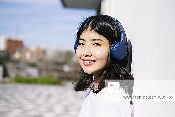 Smiling woman wearing headphones leaning on wall