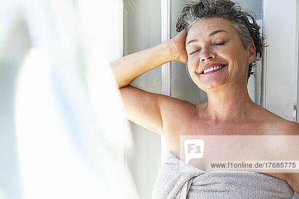 Happy woman with hand in hair standing by window at home