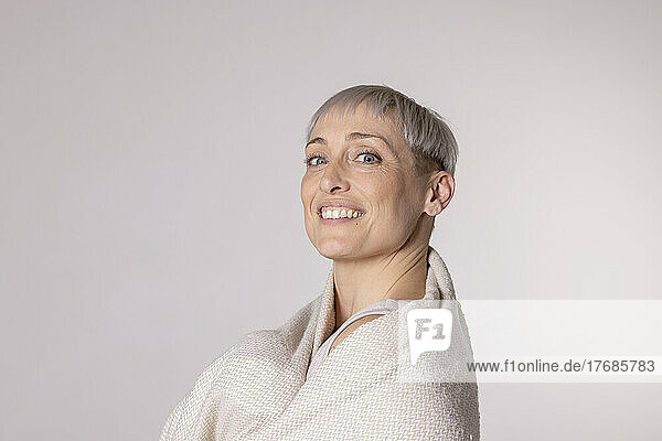 Happy woman wrapped in blanket against white background