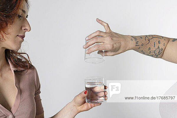 Hands of woman filling glass with water against white background