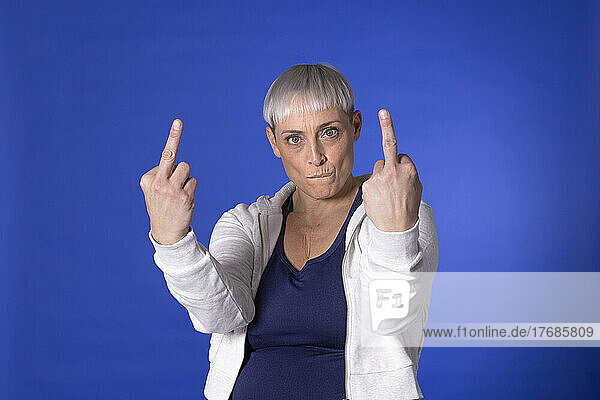 Angry woman showing obscene gesture against blue background
