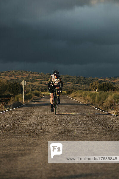 Cyclist riding bicycle on road at sunset