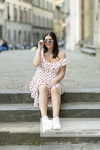 Lächelnde Frau mit Sonnenbrille sitzt auf Stufen in der Stadt